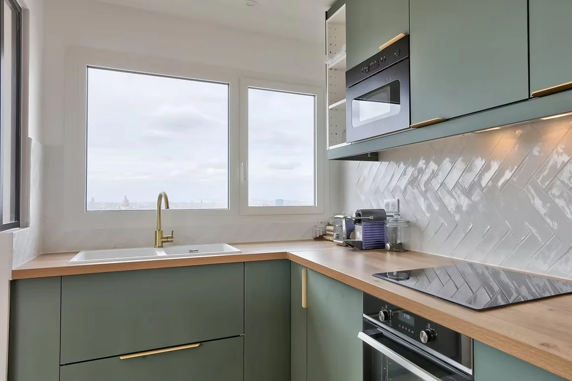 Aménagement petit appartement avec cuisine vert mat, plan bois et crédence graphique